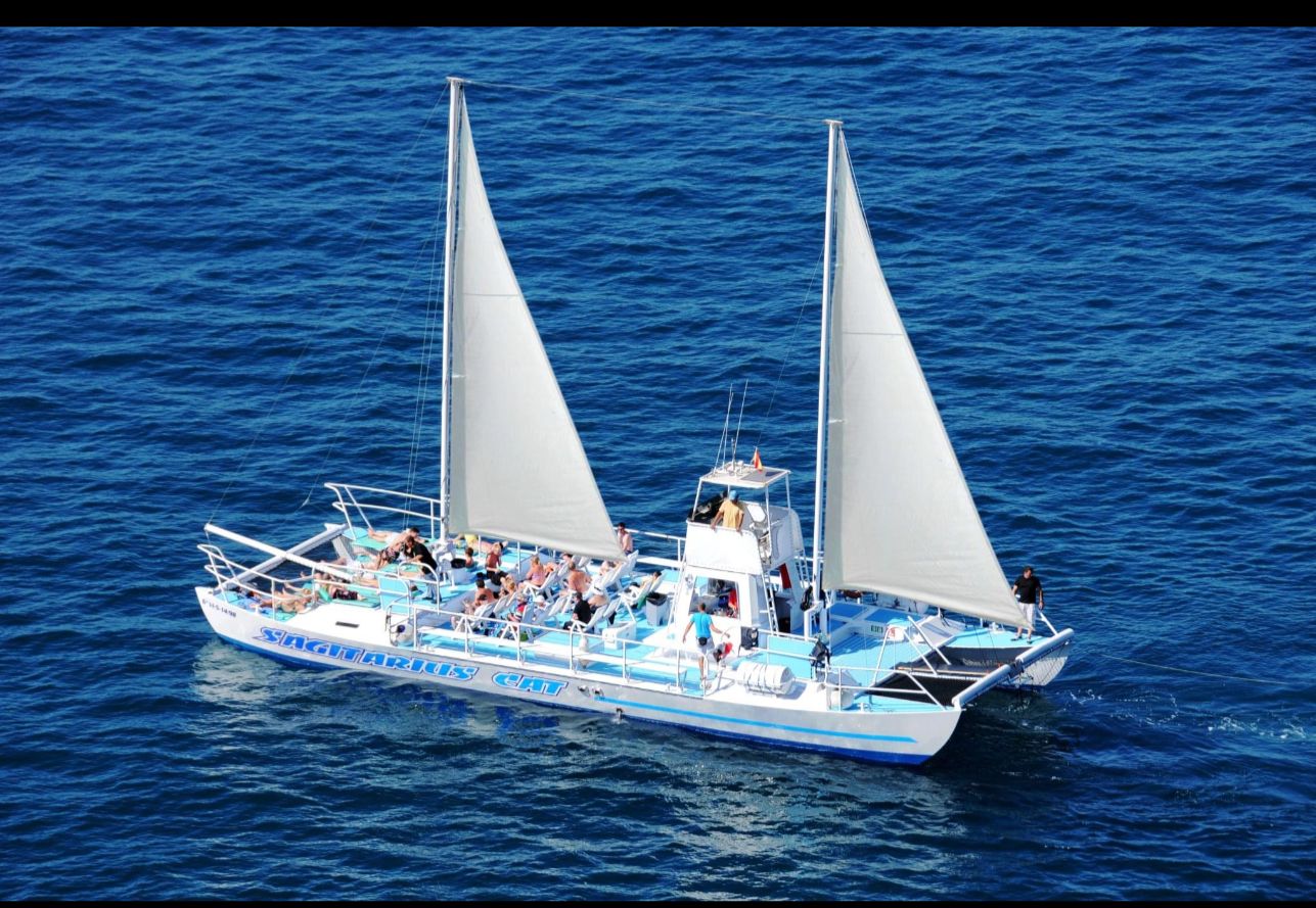 El catamarán Sagitarius Cat navegando a vela con pasaje a bordo por la costa de Mogán