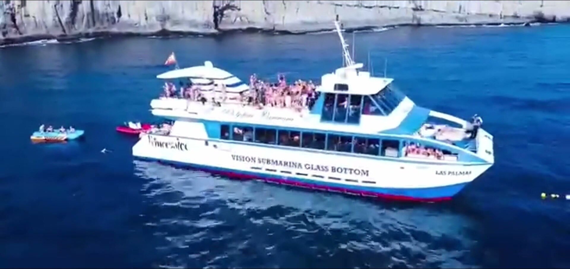 El catamarán de fondo de cristal navegando junto a los acantilados con el pasaje en cubierta