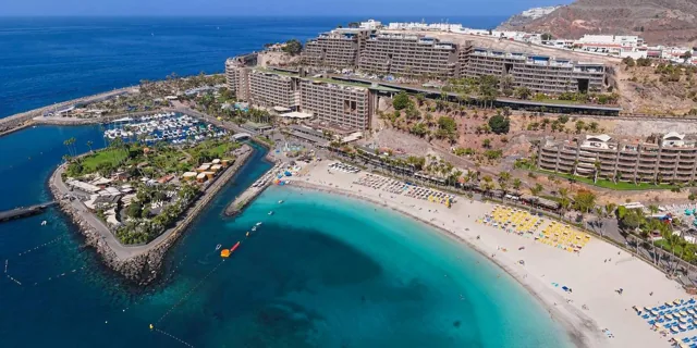 Vista aérea de una playa de arena blanca y un puerto deportivo en la costa de Mogán